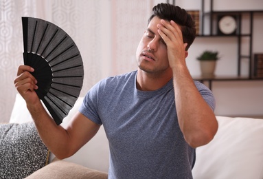 Photo of Man with hand fan sitting on sofa. Summer season