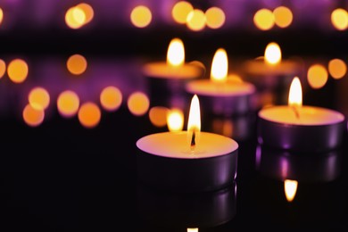 Burning violet candles on dark surface. Funeral attributes