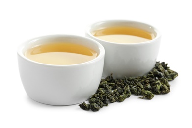 Photo of Cups of Tie Guan Yin oolong and tea leaves on white background