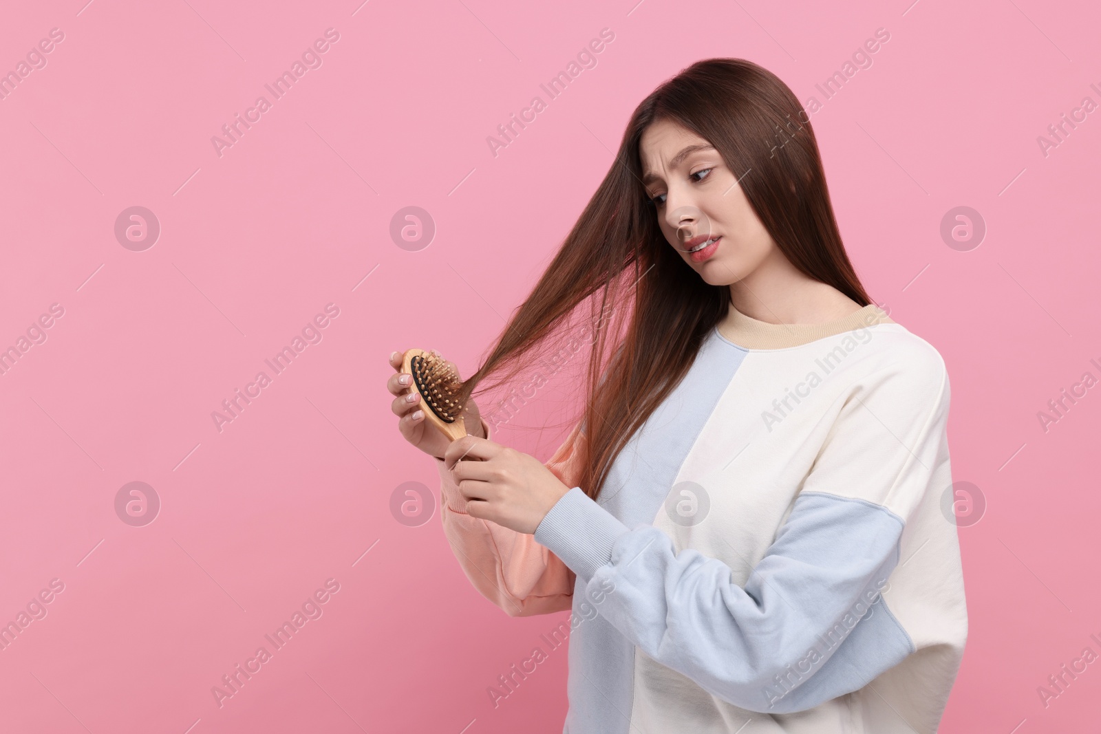 Photo of Upset woman brushing her hair on pink background, space for text. Alopecia problem