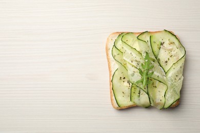 Photo of Tasty cucumber sandwich with seasoning and arugula on white wooden table, top view. Space for text