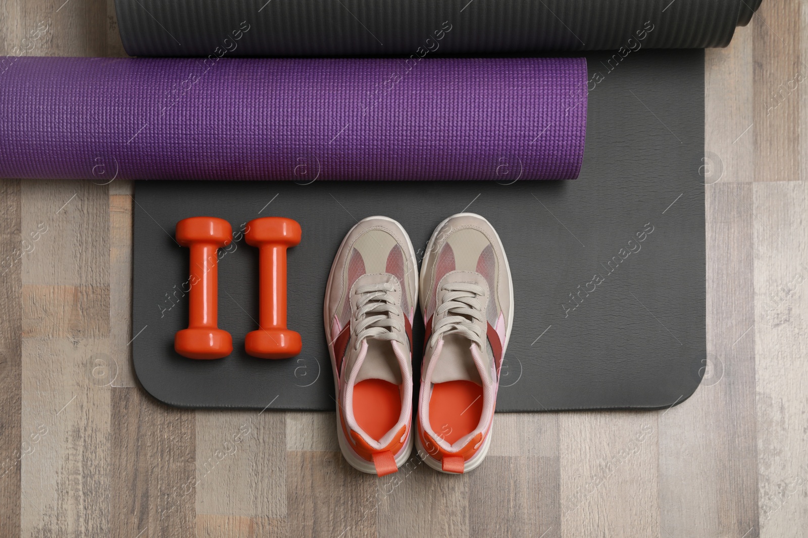 Photo of Dumbbells, sneakers and mats on wooden floor, flat lay