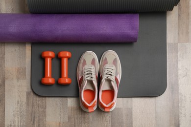 Photo of Dumbbells, sneakers and mats on wooden floor, flat lay