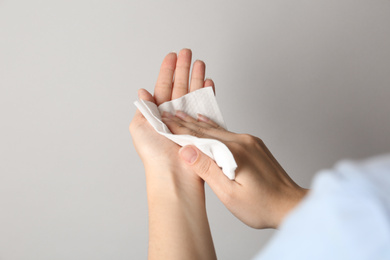 Photo of Woman cleaning hand with antiseptic wipe on light grey background, closeup. Virus prevention