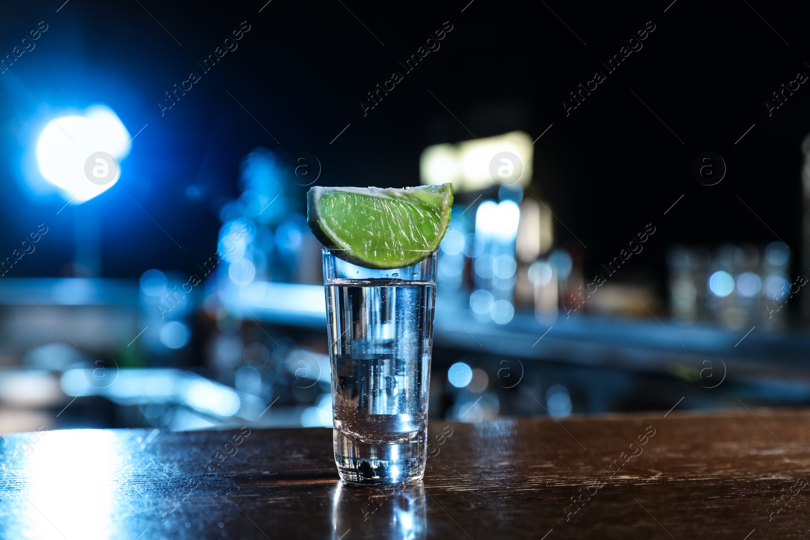 Photo of Mexican Tequila shot with lime slice on wooden bar counter