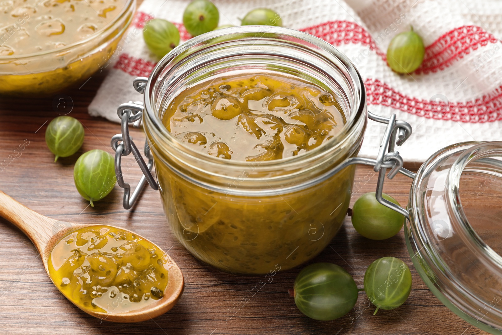 Photo of Jar, spoon with delicious gooseberry jam and fresh berries on wooden table, closeup