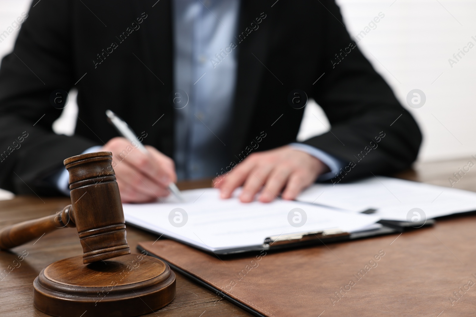 Photo of Man signing document in lawyer's office, focus on gavel