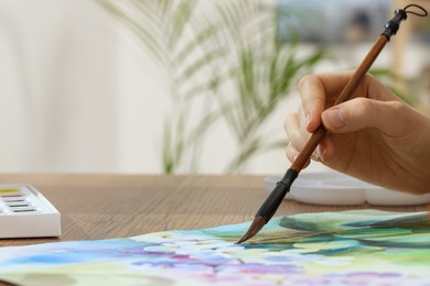 Woman painting flowers with watercolor at wooden table, closeup. Space for text