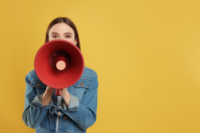 Photo of Young woman with megaphone on yellow background. Space for text