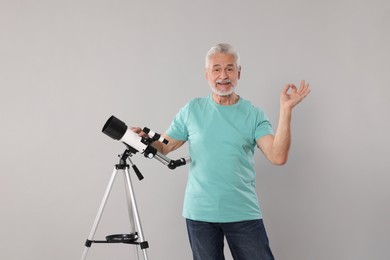 Senior astronomer with telescope showing okay gesture on grey background