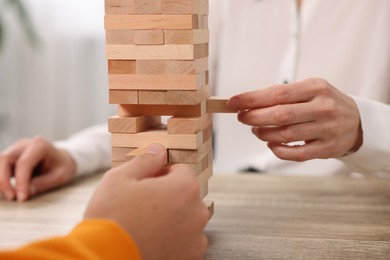 Photo of People playing Jenga tower at wooden table indoors, closeup