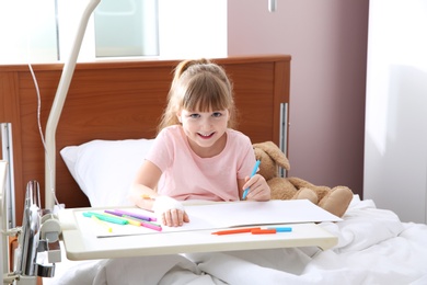 Photo of Little child with intravenous drip drawing in hospital bed