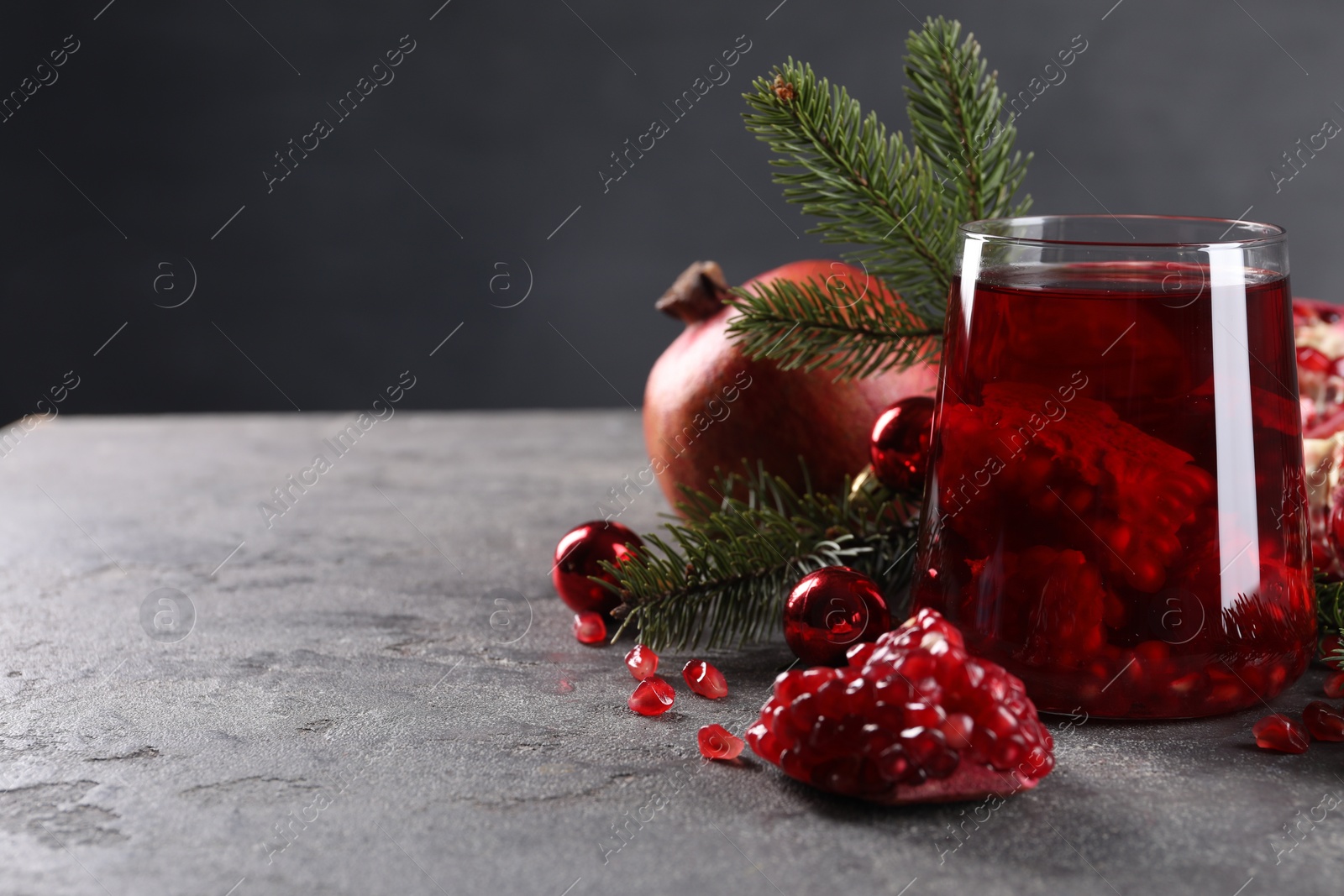 Photo of Aromatic Sangria drink in glass, Christmas decor and pomegranate grains on grey textured table, space for text
