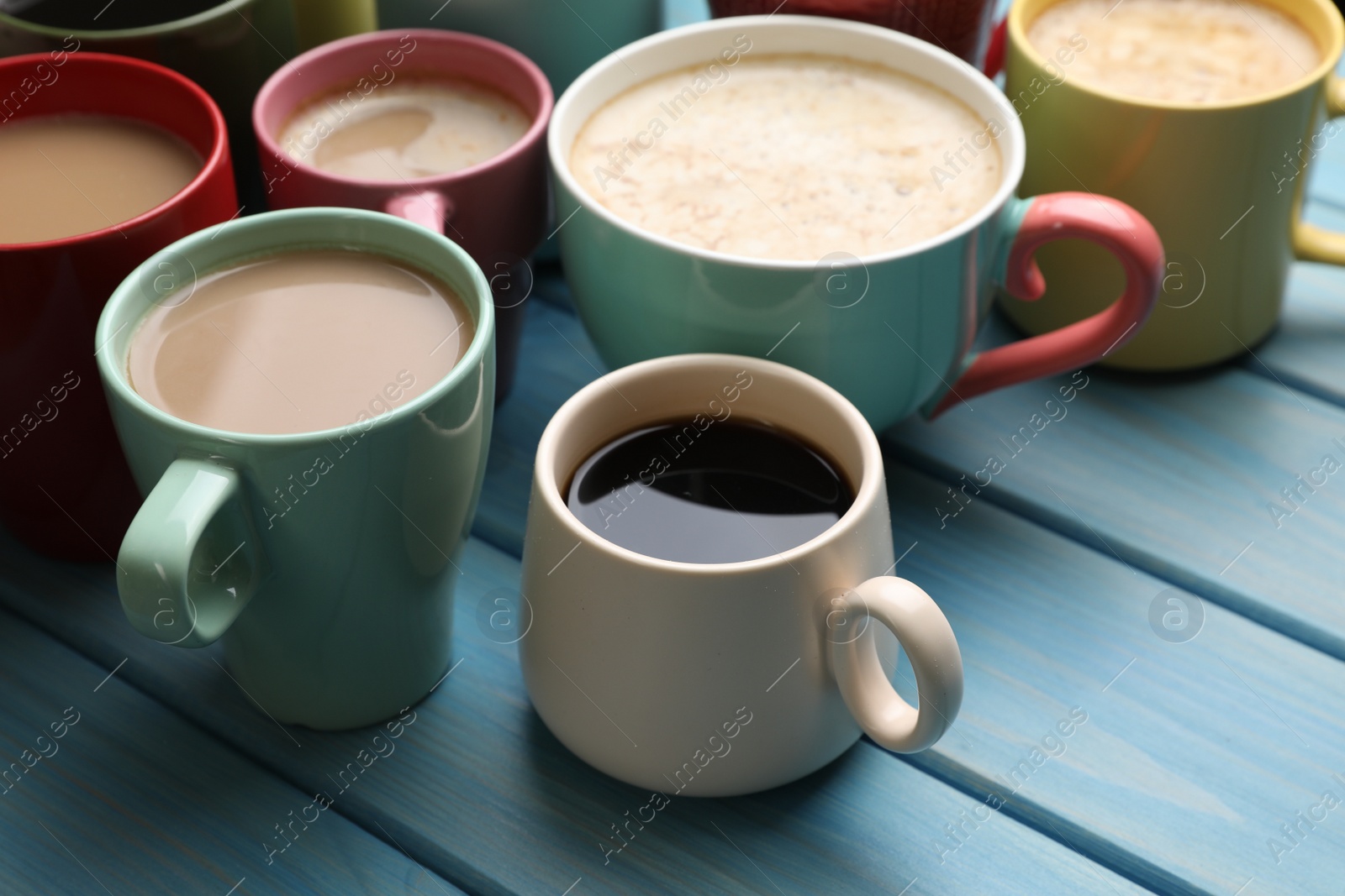 Photo of Many cups of different coffee drinks on light blue wooden table