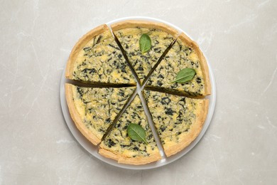 Plate of cut delicious spinach pie on light marble table, top view