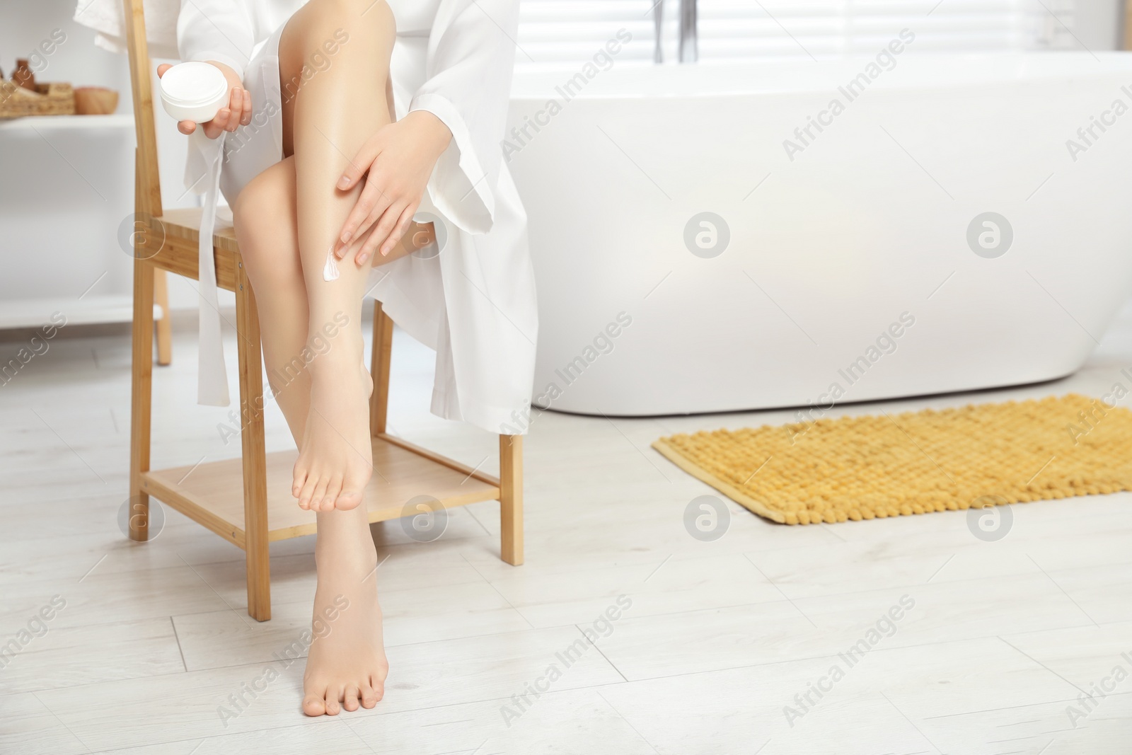 Photo of Young woman applying body cream on leg in bathroom, closeup. Space for text