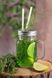 Photo of Mason jar of homemade refreshing tarragon drink with lemon slices and sprigs on wooden stump, closeup