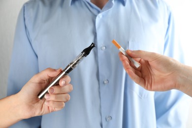 Photo of Man choosing between cigarette and vaping device on light background, closeup. Smoking alternative