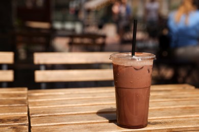 Photo of Takeaway plastic cup with cold coffee drink and straw on wooden table outdoors, space for text