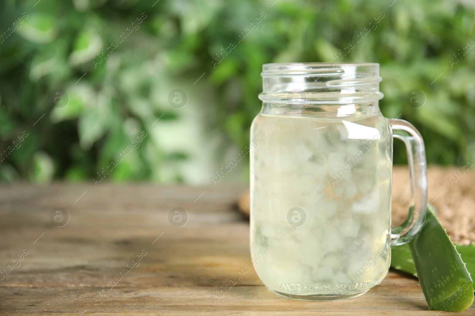 Photo of Fresh aloe drink in mason jar and leaves on wooden table, space for text