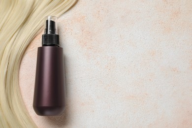 Photo of Spray bottle with thermal protection and lock of blonde hair on beige textured table, flat lay. Space for text