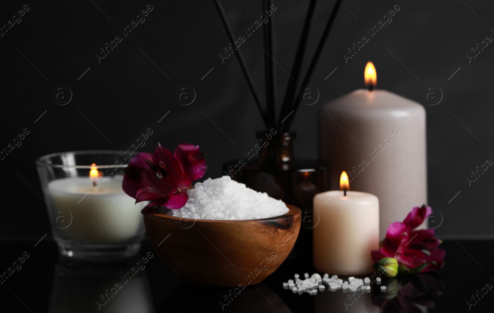 Photo of Beautiful spa composition with different care products and burning candles on mirror table against black background