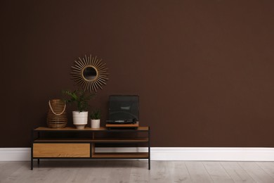 Photo of Vinyl record player and plants on table near brown wall in room, space for text. Interior design