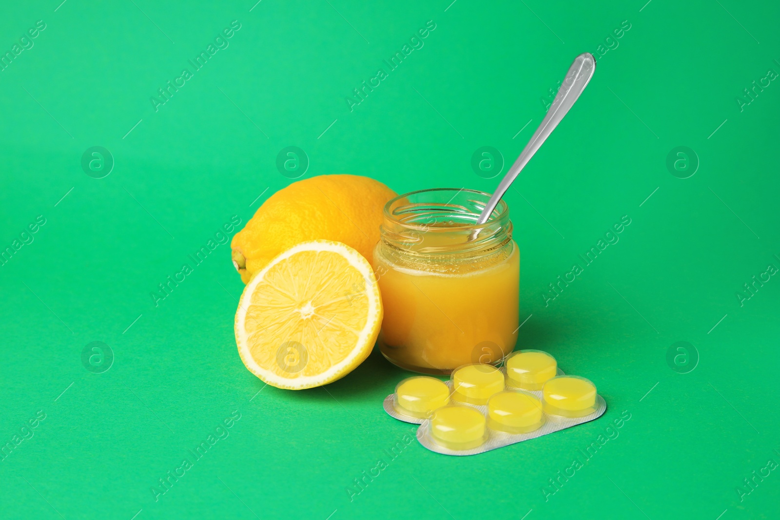 Photo of Blister with cough drops, fresh lemons and honey on green background