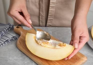 Photo of Young woman removing seeds from ripe melon with spoon at grey marble table, closeup