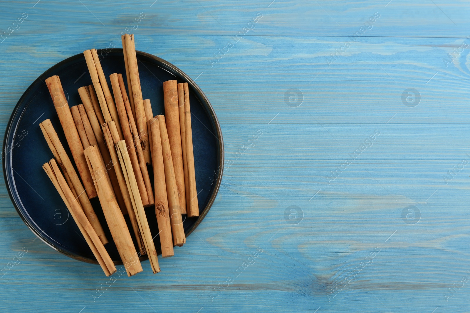 Photo of Aromatic cinnamon sticks on light blue wooden table, top view. Space for text