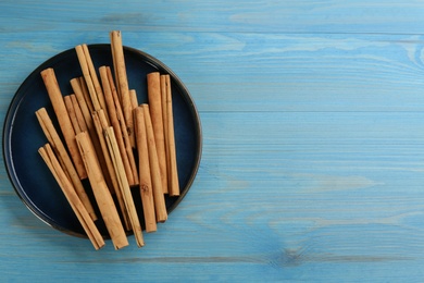 Photo of Aromatic cinnamon sticks on light blue wooden table, top view. Space for text
