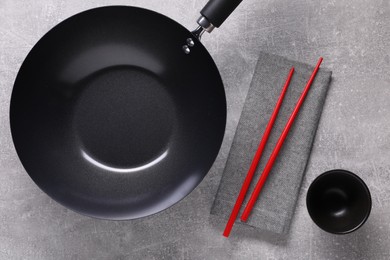 Empty iron wok, sauce bowl and chopsticks on grey table, flat lay