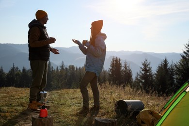 Young couple drinking coffee near camping tents in mountains