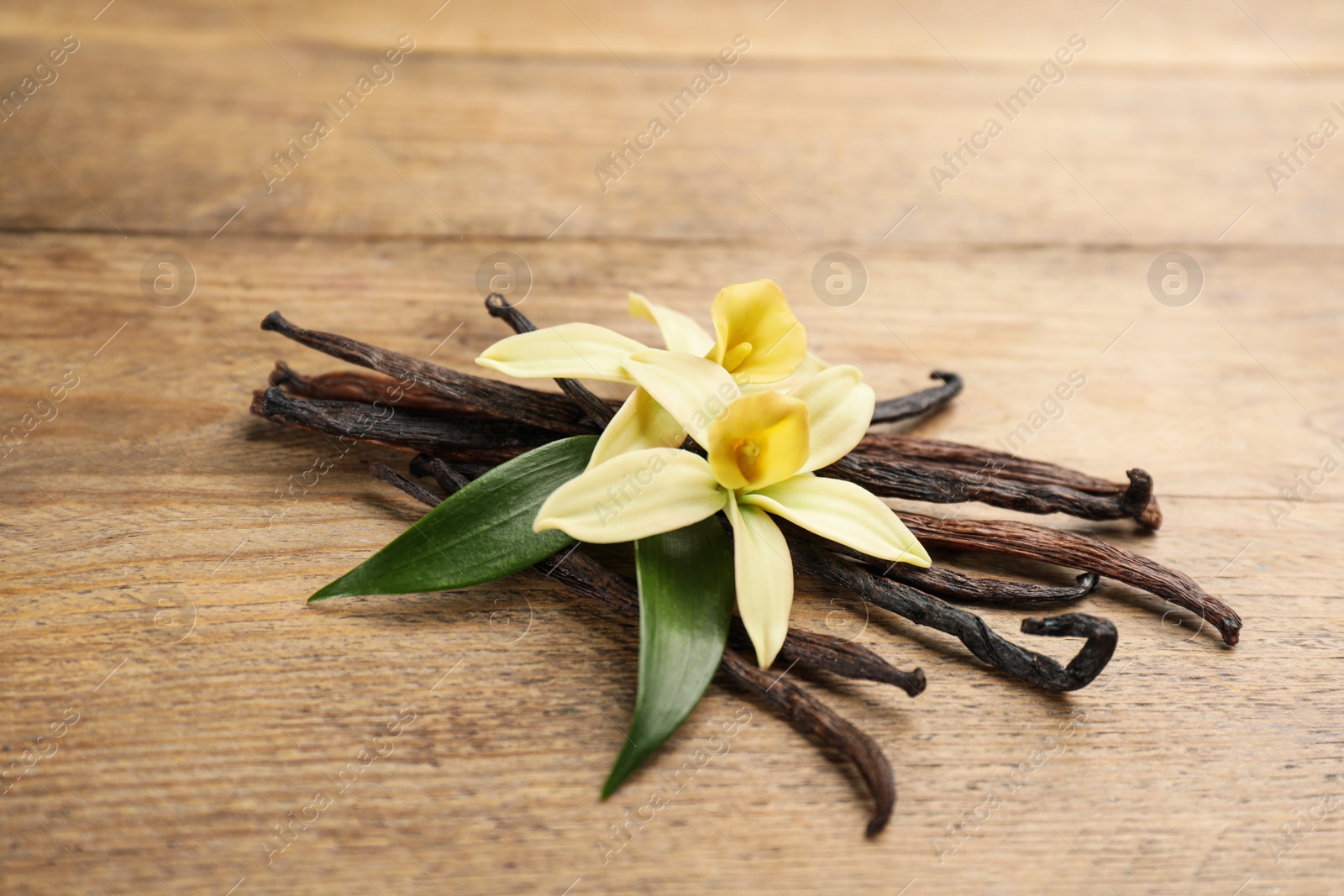 Photo of Beautiful vanilla flowers and sticks on wooden table, closeup
