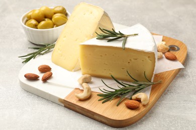 Photo of Pieces of tasty camembert cheese, rosemary, nuts and olives on grey textured table, closeup