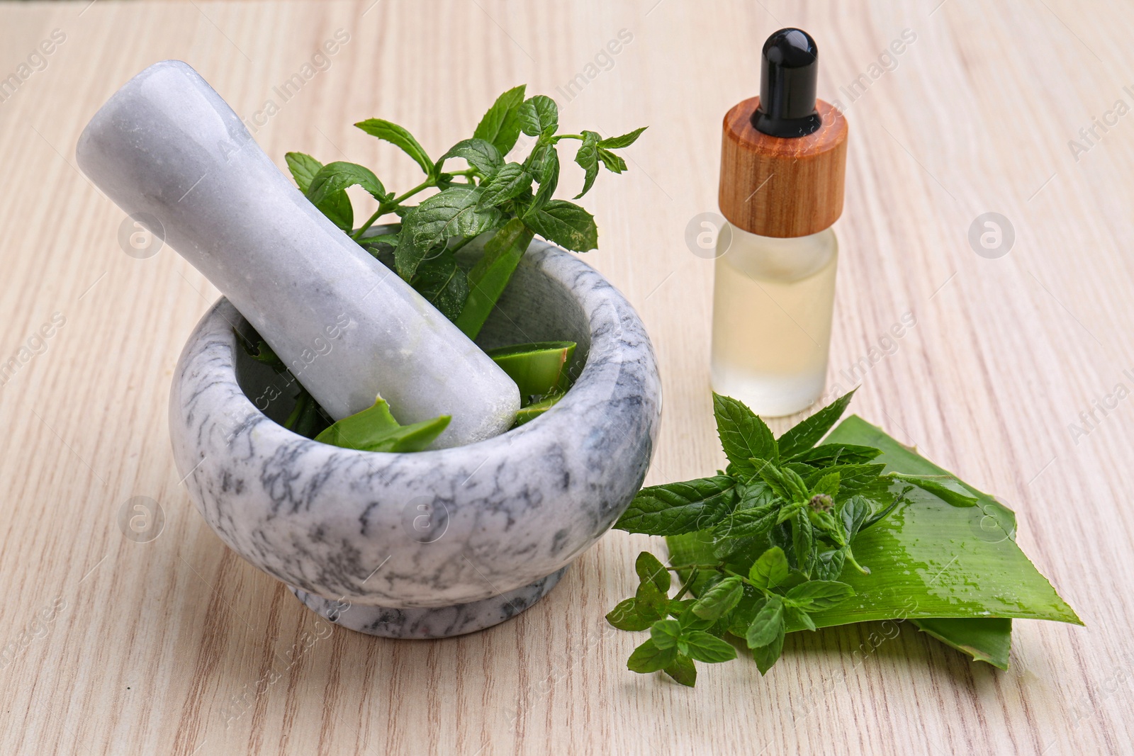 Photo of Mortar with pestle, herbs and bottle of essential oil on wooden table