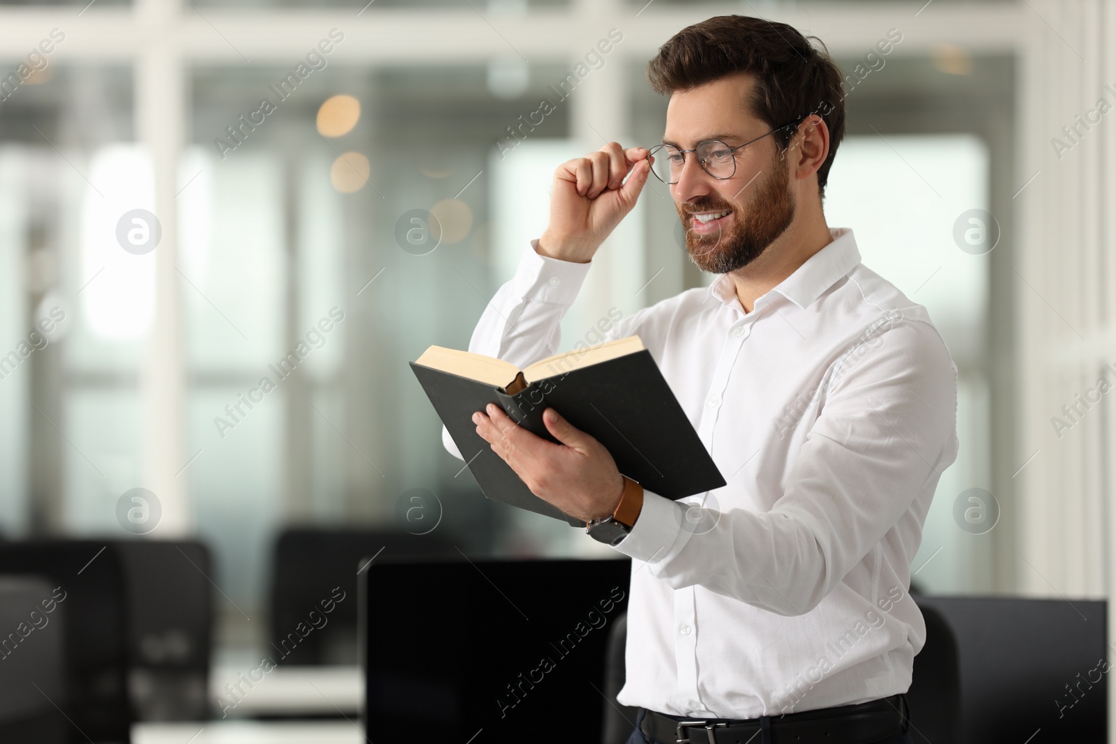 Photo of Smiling man reading book in office, space for text. Lawyer, businessman, accountant or manager