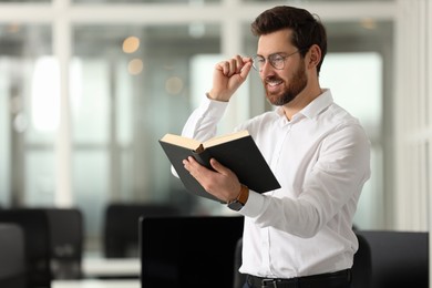 Smiling man reading book in office, space for text. Lawyer, businessman, accountant or manager