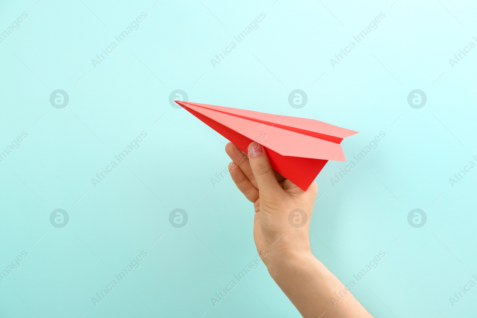 Photo of Woman holding paper plane on light blue background, closeup