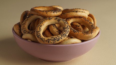 Photo of Bowl with delicious ring shaped Sushki (dry bagels) on beige background, closeup