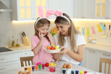 Photo of Easter celebration. Happy mother and her cute daughter with painted eggs at white marble table in kitchen