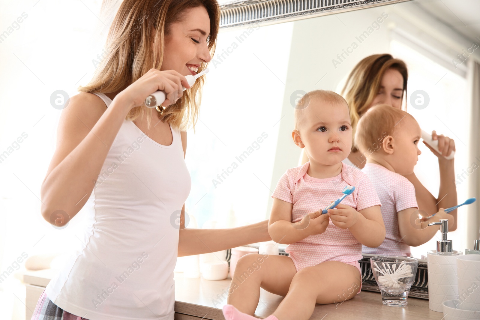 Photo of Young woman with toothbrush and daughter near mirror in bathroom