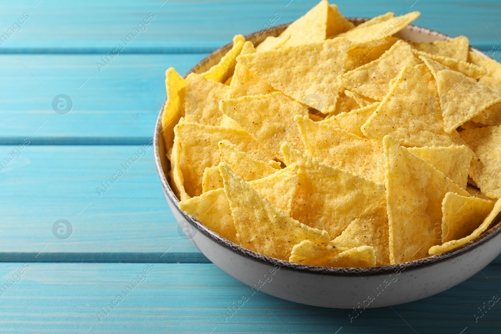 Photo of Tortilla chips (nachos) in bowl on light blue wooden table, closeup