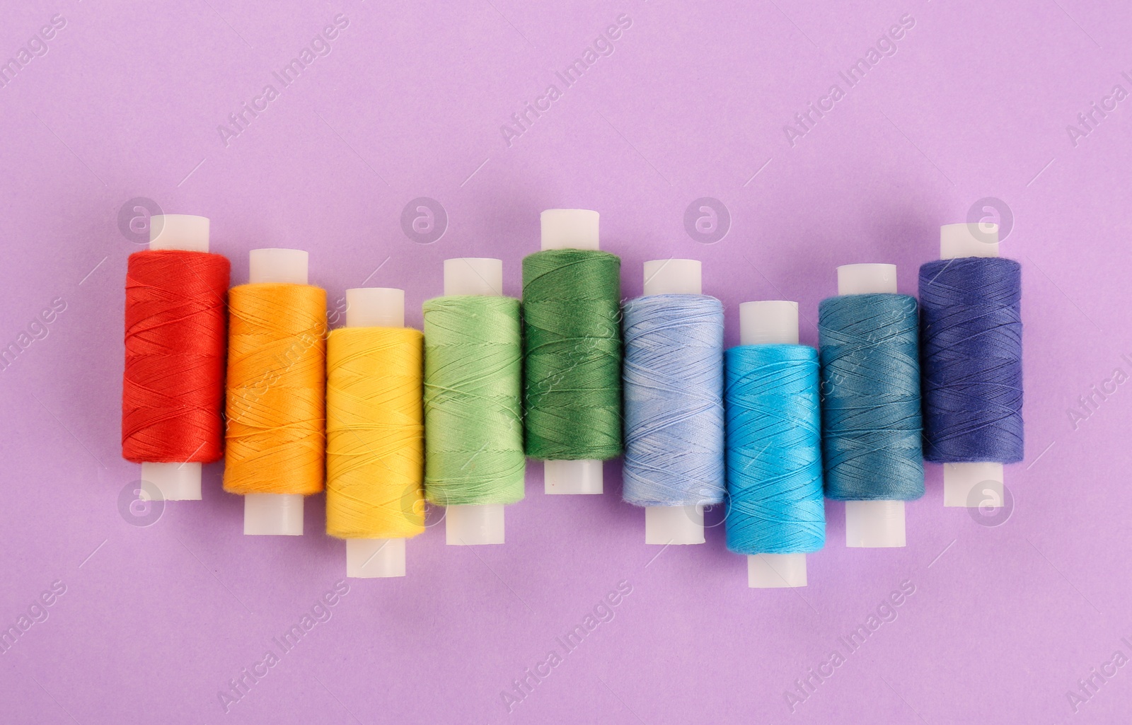 Photo of Different colorful sewing threads on lilac background, flat lay