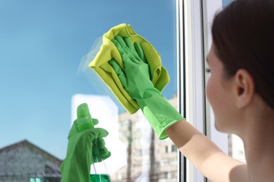 Photo of Young woman cleaning window glass with rag and detergent at home, closeup