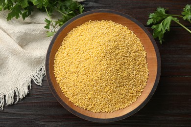 Photo of Millet groats in bowl and parsley on wooden table, top view