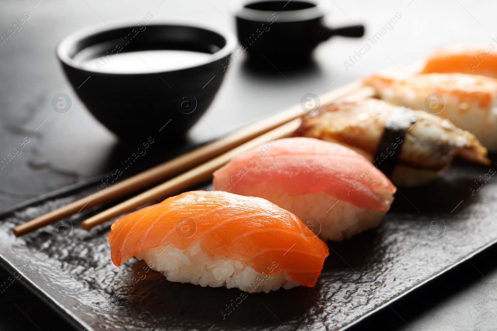 Photo of Serving board with delicious nigiri sushi and soy sauce on black table, closeup