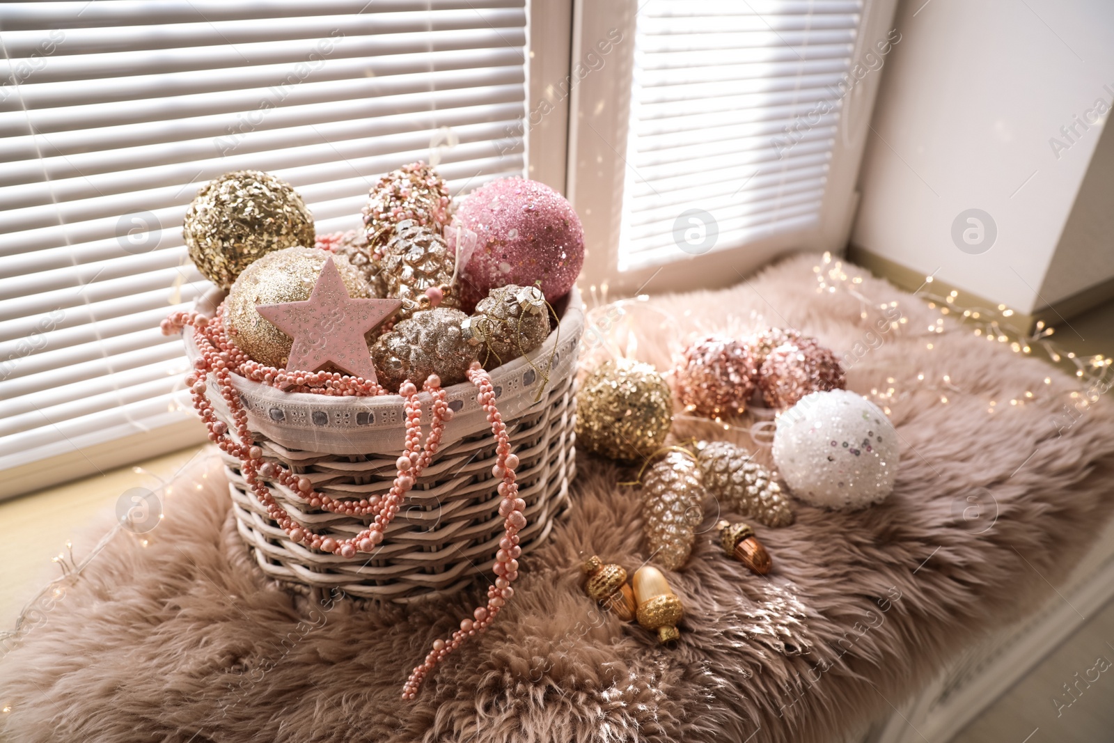 Photo of Basket with beautiful Christmas tree baubles and fairy lights on window sill indoors