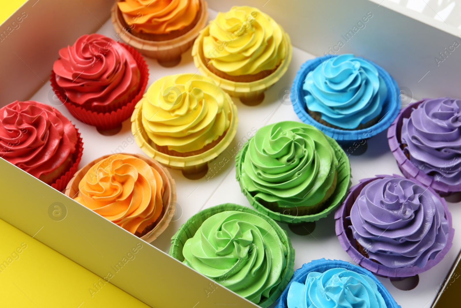 Photo of Tasty cupcakes in box on yellow background, closeup