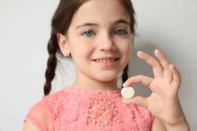 Photo of Little girl with vitamin pill against light background, focus on hand